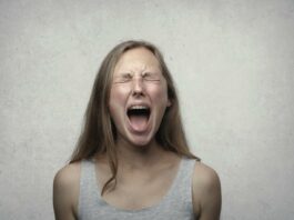 Young woman screaming with emotion, showing braces, against a gray backdrop.