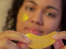 Soft focus of African American young female demonstrating eye patch in hands and looking at camera during skincare routine on beige background