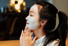 Asian woman relaxing with a face mask, practicing skincare in a cozy home environment.