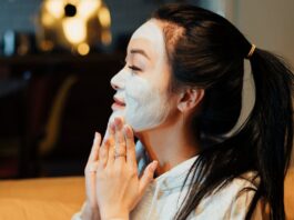 Asian woman relaxing with a face mask, practicing skincare in a cozy home environment.