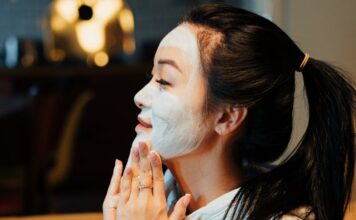 Asian woman relaxing with a face mask, practicing skincare in a cozy home environment.
